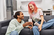 © LIGHTFIELD STUDIOS - beautiful joyful multiracial couple in homewear sitting in living room and looking at phone happily