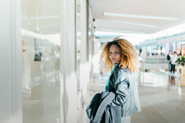 Canvas Print - A young black girl walking between stores in a shopping center window shopping. Look at camera. White background with slight overexposure