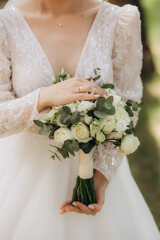 Wall Mural - young girl in a white wedding dress holds in her hands a bouquet of flowers and greenery with a ribbon