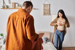 offended asian woman taking off wedding ring near husband standing with clothes in bedroom, divorce
