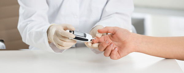 Endocrinologist checking patient's blood sugar level with digital glucometer at table, closeup. Banner design