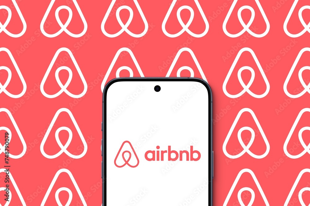 airbnb Logo is displayed on a modern smartphone, many white Airbnb Logos in front of a pink background, vacation, online marketplace for short- and long-term homestays and experiences