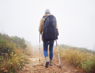 Canvas Print - Person, hiking and back in nature with trekking sticks, winter and support for fog trail in mountain. Athlete, backpack and sport gear for safety in wet environment, slippery and walking for fitness