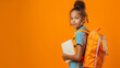 © mizan - Confident schoolgirl carrying an orange school bag, looking at the camera, standing with a textbook isolated orange background