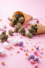 Wall Mural - Dry buds of medical marijuana lie on waffle ice cream cones on a pink background.  There are candies and marshmellos around.  Alternative medical cannabis treatment