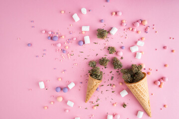 Wall Mural - Dry buds of medical marijuana lie on waffle ice cream cones on a pink background.  There are candies and marshmellos around.  Alternative medical cannabis treatment