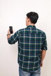 © ArvStd - Back view of young asian man standing while holding a cell phone