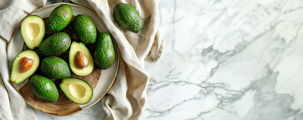 Wall Mural - Ripe avocados arranged on a white dish and wooden cutting board with cloth on white marble table with sunlight shadows. Healthy eating and diet concept banner.