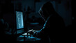 © Mongkol - A darkened room where a single computer screen casts light on the silhouette of a person typing possibly wearing a hoodie symbolizing the persistent threat of cyber attacks and cybersecurity