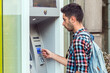 © Jelena - Young man put his credit card at the ATM on a city street.