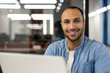 Close-up portrait of young smiling male freelancer and student working and studying in modern office, sitting at laptop and looking at camera