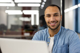 Fototapeta  - Close-up portrait of young smiling male freelancer and student working and studying in modern office, sitting at laptop and looking at camera
