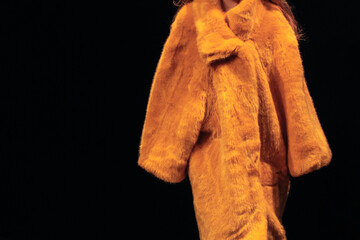 Sticker - Bright yellow women's fur coat on a black background. Winter fashionable look