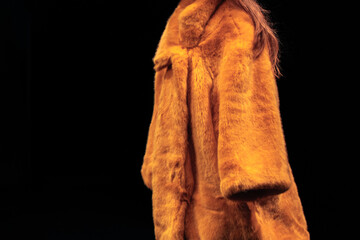 Sticker - Bright yellow women's fur coat on a black background. Winter fashionable look. Side view