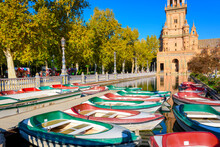 Green And Red Boats For Hire Sit In The Water Ready For Visitors In The Morning At The Plaza De Espana Public Square And Park In The Andalusian City Of Seville, Spain.