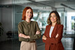 © insta_photos - Happy confident professional business women of young and middle age posing at work looking at camera. Two smiling confident ladies standing arms crossed in office. Women power partnership, portrait.