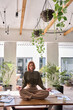 © insta_photos - Happy serene calm young business woman employee with red hair sitting on work desk meditating, doing yoga breathing exercises for no stress in green cozy office. Candid vertical photo.
