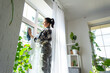 © Ольга Симонова - Woman manually washes the window of the house with a rag with spray cleaner and mop inside the interior with white curtains. Restoring order and cleanliness in the spring, cleaning servise