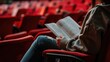 Young woman reading in empty red theater seats, immersed in story