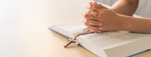 Poster - Asian male folded hand prayed on holy bible book while holding up a pendant crucifix. Spiritual, religion, faith, worship, christian and blessing of god concept. Blurring background. Burgeoning.