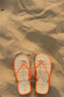 A pair of orange flip flops are on a sandy beach