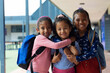 Three biracial girls smile outside a school, the youngest held by the other two