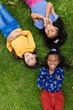 Three biracial girls are lying on the grass in school, smiling and looking upwards