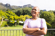 Senior biracial woman stands confidently outdoors, arms crossed, smiling, with copy space