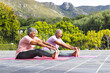 Senior African American woman and senior biracial woman are smiling while doing yoga outdoors