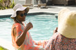 Senior African American woman sips a drink by the pool, wearing a sunhat and sunglasses