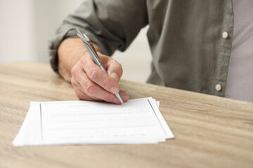 Wall Mural - Senior man signing Last Will and Testament at wooden table indoors, closeup