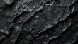 A crumpled paper background displays a soft black creating a visually intriguing and unique texture. Black paper background with folds and wrinkles in a rustic feel.