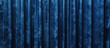 A blue curtain made of velvet fabric hangs against a dark black background. The contrast between the vibrant blue and the deep black creates a striking visual impact. The curtain is perfect for adding