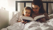 mother and child daughter reading book in bed before going to sleep at night