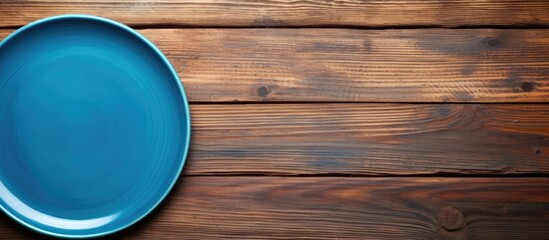 Canvas Print - A blue ceramic plate is placed neatly on top of a wooden table. The plate stands out against the natural brown hue of the table, creating a simple yet eye-catching contrast.