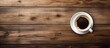 A birds eye view of a simple ceramic cup filled with steaming hot coffee resting on a worn wooden table surface. The warm brown tones create a cozy and inviting atmosphere.