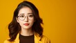Capture the image of an Asian woman wearing glasses, posing confidently against a vibrant yellow background. 
