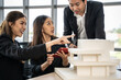 © Bavorndej - Young asian man presents a building model to team at the office. They discuss building design together in the office.