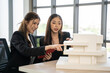 © Bavorndej - Two engaged female business colleagues using a tablet to review a project beside an architectural model in an office setting.