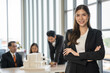 © Bavorndej - Portrait of young beautiful woman looking to camera in meeting room. She looking to camera with happy expression in her office with team. Business people concept.