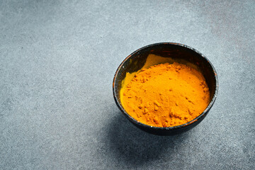 Wall Mural - Spices. Turmeric powder in a black ceramic bowl on a concrete gray background.