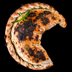 Sticker - Neapolitan cuisine closed pizza calzone with basil and spices isolated on black.