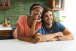 Diverse couple smiles warmly, leaning on a kitchen counter