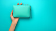 Female hand holding a turquoise clutch on a blue background with  copy space. generative ai