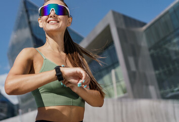 Energetic woman with sports watch and futuristic sunglasses running in urban setting.