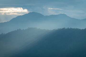 Wall Mural - Sun rays filter through the clouds in hills of the valley illuminated by the sun's rays filtering through the clouds