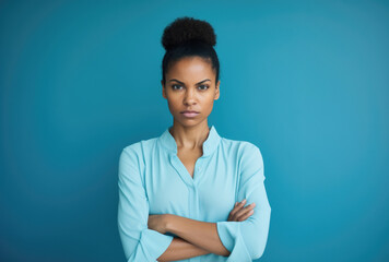 Determined woman with a top bun in a light blue blouse, exuding confidence against a matching blue background.