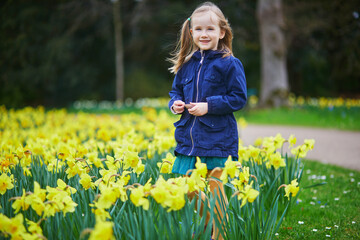 Wall Mural - Adorable preschooler girl enjoying nice spring day in park during jonquils blooming season