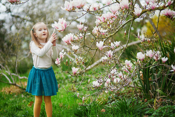 Wall Mural - Adorable preschooler girl enjoying nice spring day in park during magnolia blooming season