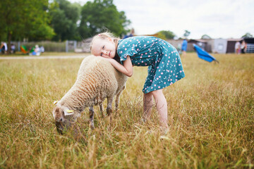 Wall Mural - Adorable little girl playing with sheep at farm